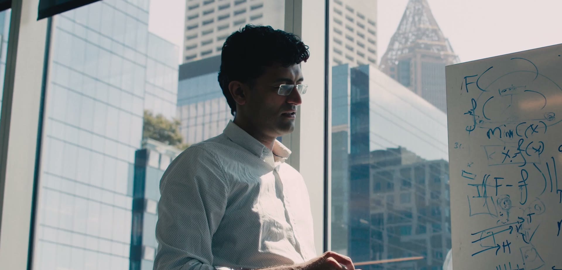 Animesh Garg by a window overlooking the city, next to a whiteboard.